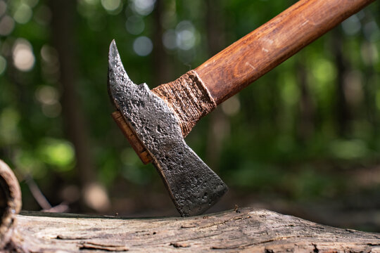 Handmade forged steel axe on ancient wooden log in forest close up.
