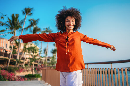 Beautiful woman joyfully raises her arms high celebrating life against a vibrant tropical background
