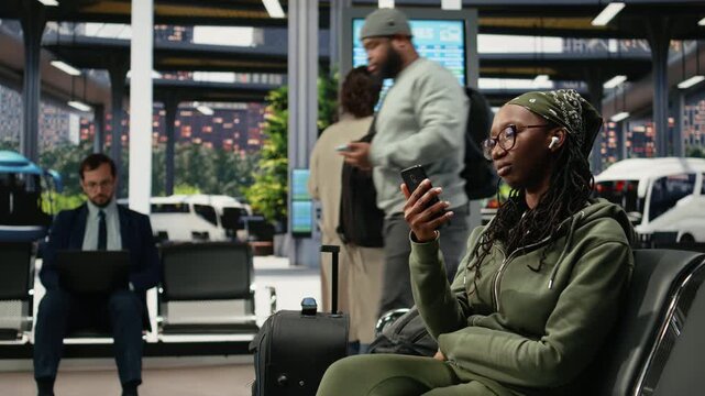 Woman sends an audio message through her smartphone in a bus terminal while waiting, speaking into the phone speaker with earphones before departure.