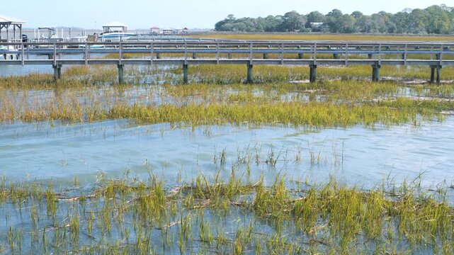 Flowing salt water tidal creek at a very high tide with marsh grass, and a dock boardwalk in the background, 4k, slow motion.