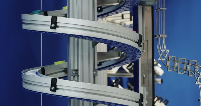 Spiral conveyor rotates within vertical automated transporting system. Curved mechanism guides continuous factory flow between production levels on plant
