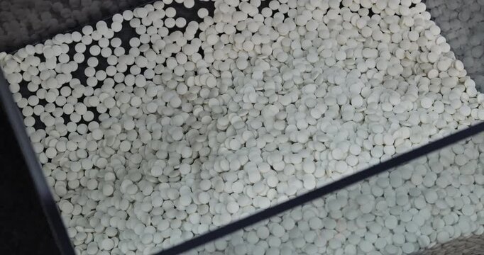 White tablets fall into collection hopper joining processed medicine batch. Automated feeder transfers fresh units from upper pharmaceutical production stage
