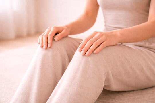 Person resting hands upon knees while wearing soft beige lounge clothing, calm posture fingers skin, relaxed limbs, neutral fabric textile color.