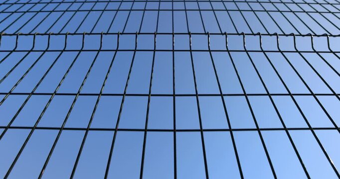 Dark wire grid fence on blue sky background, section of metal mesh fencing barrier installed outside for security and protection