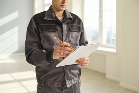 Inspector contractor worker with clipboard checklist. Writes notes during inspection in bright interior, documenting tasks and renovation progress. Professional construction site assessment concept.