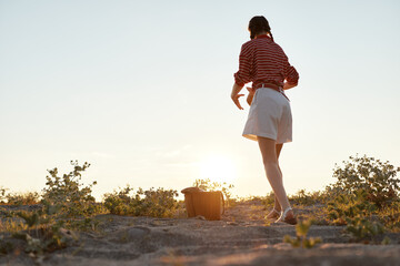 Fototapeta premium A woman in a striped top and white shorts walks away across a sunlit landscape, capturing a carefree, casual summer lifestyle in the outdoors.