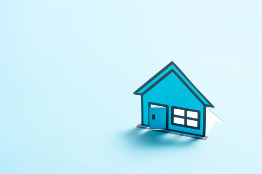 A minimalist blue miniature house model isolated on a light background, symbolizing homeownership, real estate, housing, property and residential architecture.