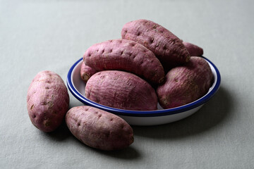 Fototapeta premium Raw purple sweet potatoes in a bowl on cotton fabric background
