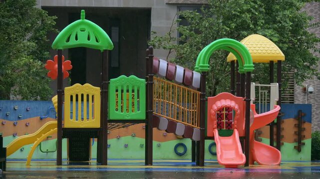 Colorful outdoor children playground equipment standing wet on residential compound grounds amid rainy weather