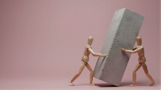 Two wooden figures push a heavy concrete block together, symbolizing teamwork.
