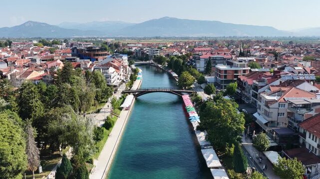 Aerial drone view of Struga in North Macedonia with Black Drin River flowing into crystal clear Lake Ohrid, boats, sunny summer landscape, waterfront buildings and scenic city panorama