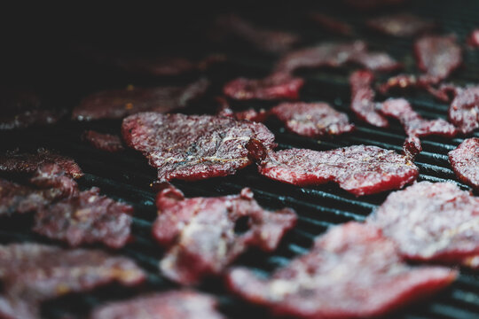 Thin slices of round steak dry slowly on a pellet grill smoker, their deep red color and crisp texture revealing the final stage of homemade beef jerky creation.