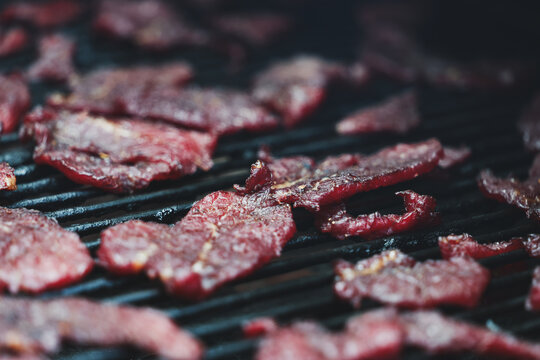Thin slices of round steak dry slowly on a pellet grill smoker, their deep red color and crisp texture revealing the final stage of homemade beef jerky creation.