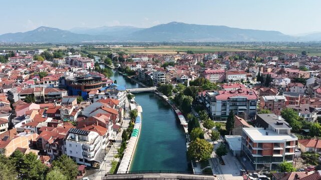 Aerial drone view of Struga in North Macedonia with Black Drin River flowing into crystal clear Lake Ohrid, boats, sunny summer landscape, waterfront buildings and scenic city panorama