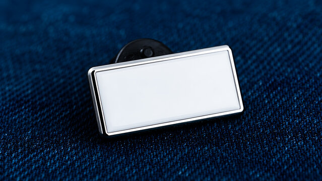 Silver rectangular photo frame pin with blank white insert displayed on deep blue denim fabric texture. Corporate identity badge pin, customizable company logo holder