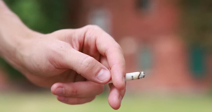 Man flicking ash from cigarette outdoors, closeup. Camera moving in