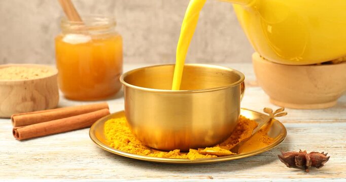Pouring golden milk turmeric latte into cup at old wooden table, closeup