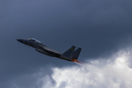 Side view of a F-15 Eagle climbing  with afterburners on, against clouds