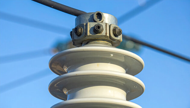 Close-up of Electrical Insulator: A ceramic electrical insulator on a power line, designed to prevent current leakage and ensure safe transmission of electricity, against a clear blue sky.