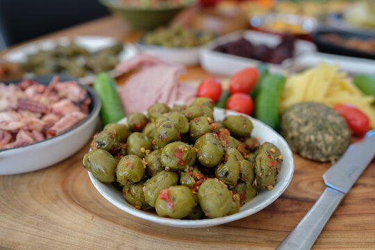 Green olives, mediterranean food, appetizer, meze, healthy snack, gourmet deli, tapas spread featuring seasoned olives, fresh vegetables, and deli meats on a rustic wooden table.