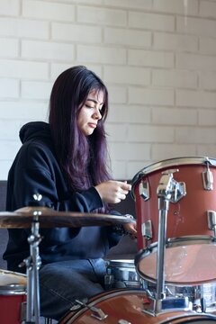 A young woman sitting at a drum set, practicing at home
