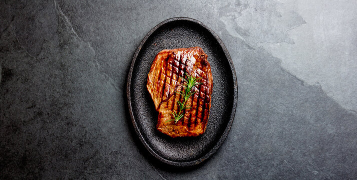 Grilled beef steak on black cast iron plate. Background with copy space. Barbecue, bbq meat beef tenderloin. Top view, slate background