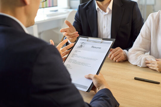 Interview with recruiter as candidates present resume. HR hiring meeting in bright office during job discussion. Application review shows fit and skills. Clear career and employment concept.
