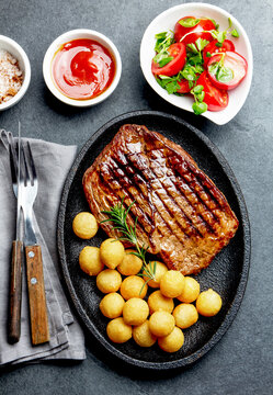 Grilled beef steak served on cast iron plate with tomato salad and potatoes balls. Barbecue, bbq meat beef tenderloin. Top view, slate background