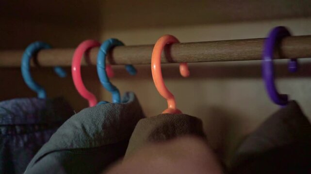 Close up of colorful clothes hangers on wooden closet rod, hand selecting clothes from wardrobe, morning routine and fashion choice concept.