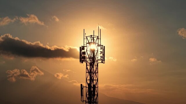 Communication tower against bright orange sunset sky, silhouette shot. Telecom, network, and wireless technology concept, evening cloud footage.