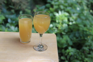 Glasses of orange juice on a wood table in the garden with a space for writing. Fruit juice in summer with a green background and vegetation. Refreshment and natural juice in orange color. © Martine