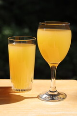 Glasses of orange juice on a wood table in the garden. Fruit juice in summer with a green background and vegetation. Refreshment and natural juice in orange color. © Martine
