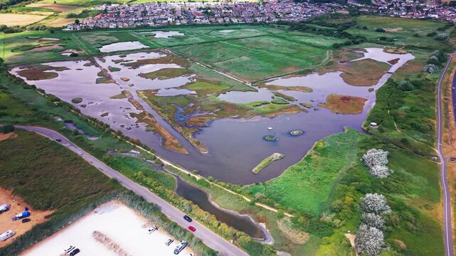 Drone shot over RSPB Lodmoor's wetland lagoons, reed beds and nesting islands with Weymouth beyond.