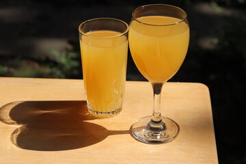 Glasses of orange juice on a wood table in the garden. Fruit juice in summer with a green background and vegetation. Refreshment and natural juice in orange color. © Martine