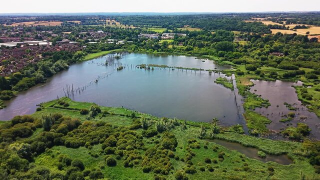 Drone pulls back from Fishlake Meadows' open lake, revealing wetland scrub and Romsey's rooftops beyond.
