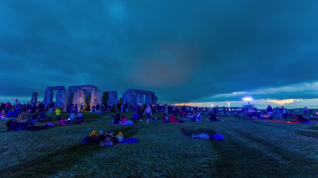 Wide shot of crowds resting and camped on the ground at Stonehenge overnight, awaiting the solstice sunrise.