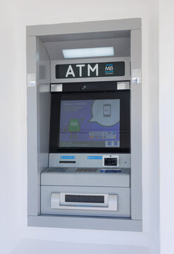202608-24 Lisboa, Portugal - Multibanco ATM embedded in a white wall, featuring the ATM and MB Multibanco branding. The machine includes a screen, card reader, keypad, cash dispenser, and contactless 
