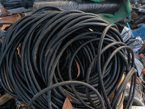 Coil of black plastic HDPE pipe hose for agricultural drip irrigation system outdoors on a farm.