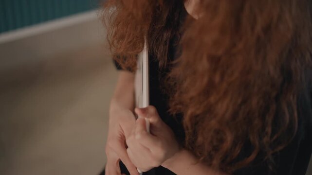 Woman's hands and forearms hold thin white booklet or stack of cards against chest while fingers adjust paper edge and thumb presses back, showing steadying, turning, and preparing to open