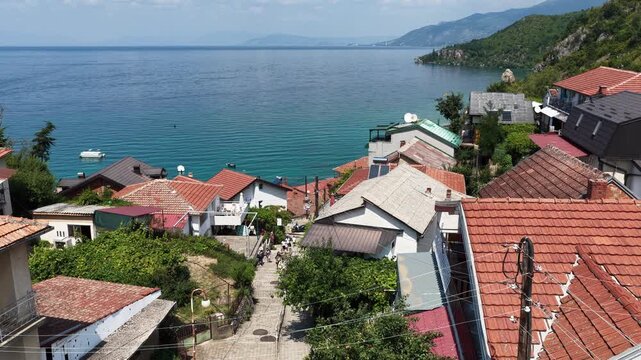 Aerial drone view of Trpejca village on Lake Ohrid, North Macedonia, traditional buildings, crystal clear turquoise lake water, rocky shoreline and beautiful lakeside beach