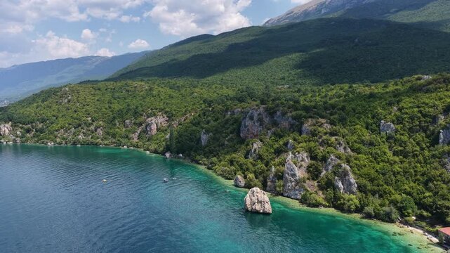 Aerial drone view of Trpejca village on Lake Ohrid, North Macedonia, traditional buildings, crystal clear turquoise lake water, rocky shoreline and beautiful lakeside beach