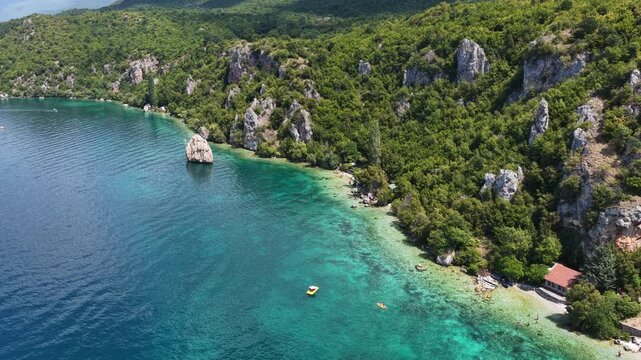 Aerial drone view of Trpejca village on Lake Ohrid, North Macedonia, traditional buildings, crystal clear turquoise lake water, rocky shoreline and beautiful lakeside beach