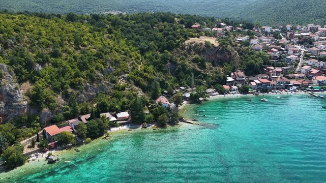 Aerial drone view of Trpejca village on Lake Ohrid, North Macedonia, traditional buildings, crystal clear turquoise lake water, rocky shoreline and beautiful lakeside beach