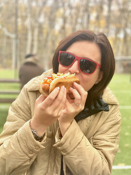 Young Woman wearing sunglasses eating hot dog outside on a street