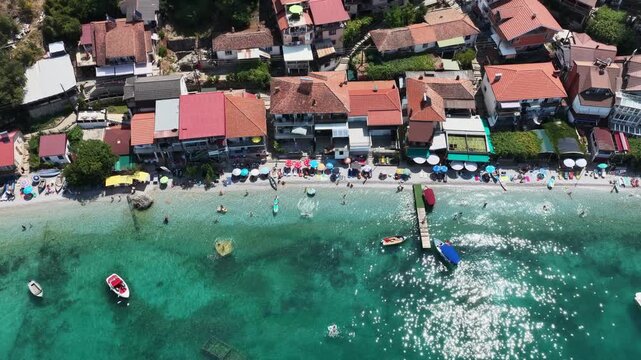 Aerial drone view of Trpejca village on Lake Ohrid, North Macedonia, traditional buildings, crystal clear turquoise lake water, rocky shoreline and beautiful lakeside beach