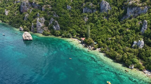 Aerial drone view of Trpejca village on Lake Ohrid, North Macedonia, traditional buildings, crystal clear turquoise lake water, rocky shoreline and beautiful lakeside beach