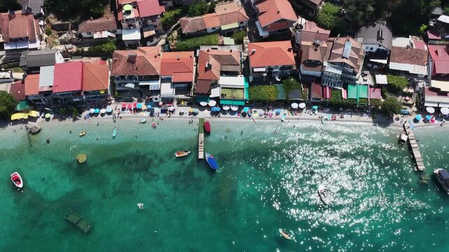 Aerial drone view of Trpejca village on Lake Ohrid, North Macedonia, traditional buildings, crystal clear turquoise lake water, rocky shoreline and beautiful lakeside beach
