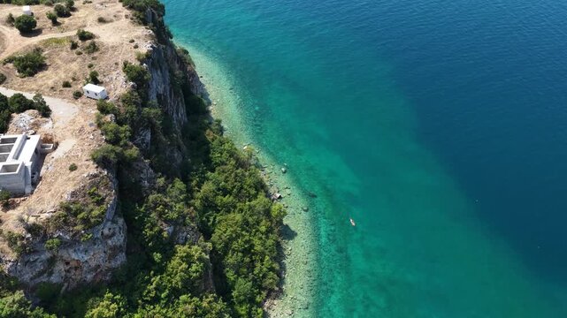 Aerial drone view of Trpejca village on Lake Ohrid, North Macedonia, traditional buildings, crystal clear turquoise lake water, rocky shoreline and beautiful lakeside beach