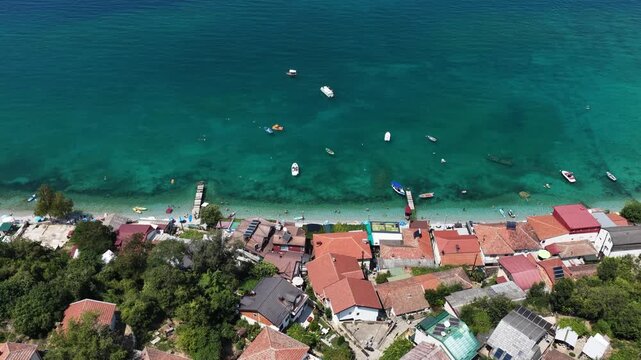 Aerial drone view of Trpejca village on Lake Ohrid, North Macedonia, traditional buildings, crystal clear turquoise lake water, rocky shoreline and beautiful lakeside beach