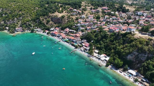 Aerial drone view of Trpejca village on Lake Ohrid, North Macedonia, traditional buildings, crystal clear turquoise lake water, rocky shoreline and beautiful lakeside beach